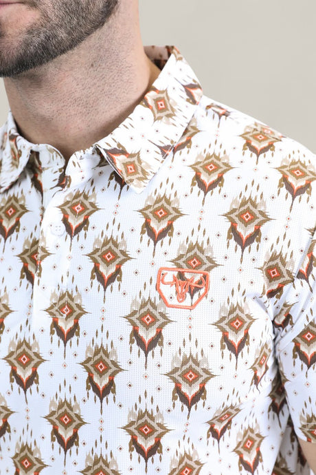 A close-up of a man in the Mens Performance Fabric Modern Fit Stretch Aztec Print White Polo (PGP10870), featuring a brown and orange geometric pattern and an embroidered bull head emblem. Only his lower face and upper torso are visible.