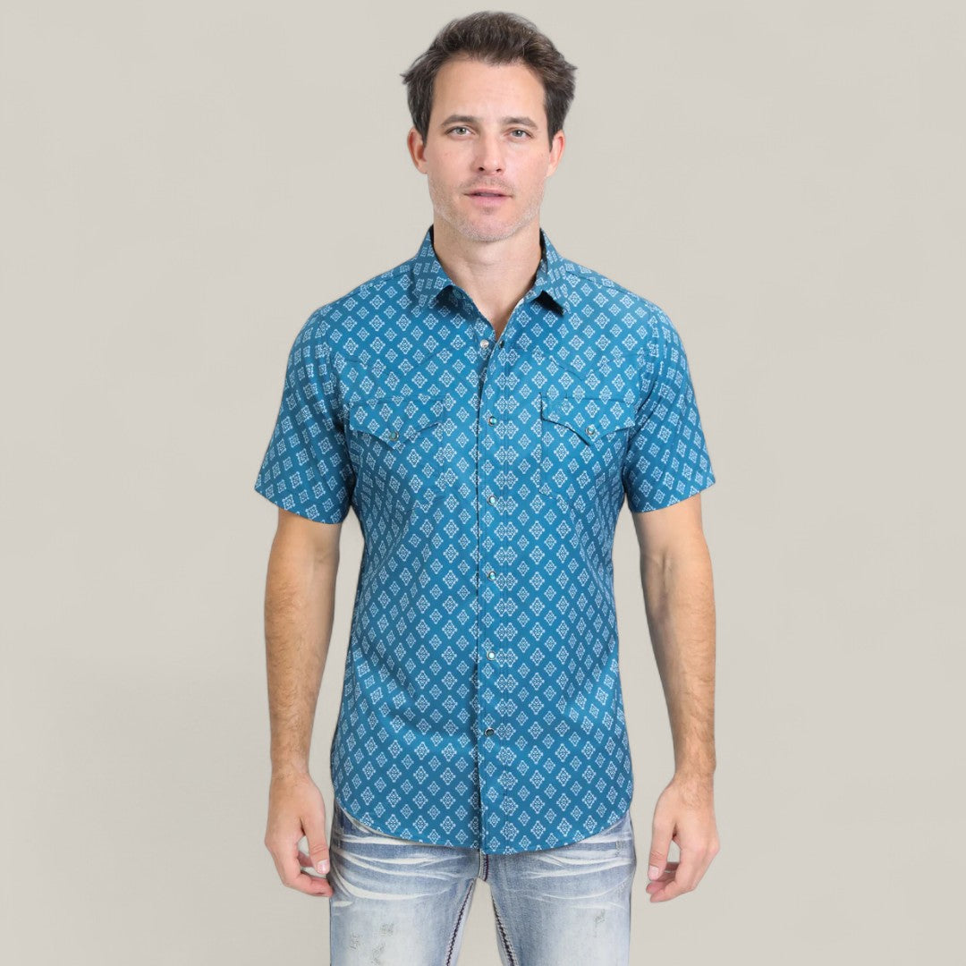 A man with short brown hair wears the Mens Performance Western Short Sleeve Aztec Print Blue Shirt - PGW10632 and light blue jeans, standing against a plain light gray background.