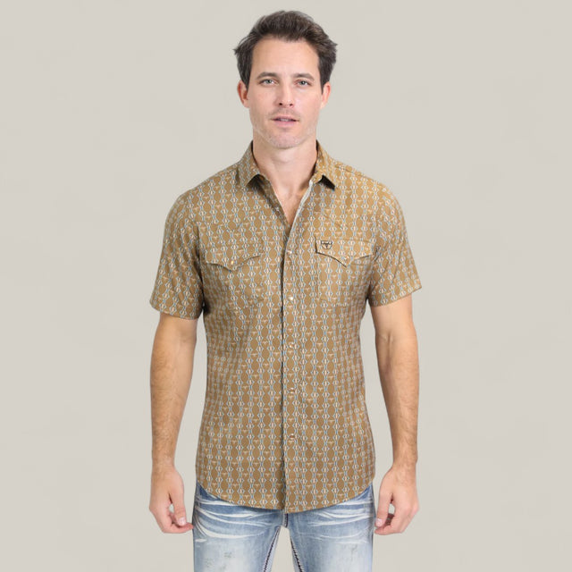 A man stands facing forward, wearing the Mens Performance Western Short Sleeve Aztec Print Camel Shirt (PGW10645) with faded blue jeans, set against a plain light beige background.