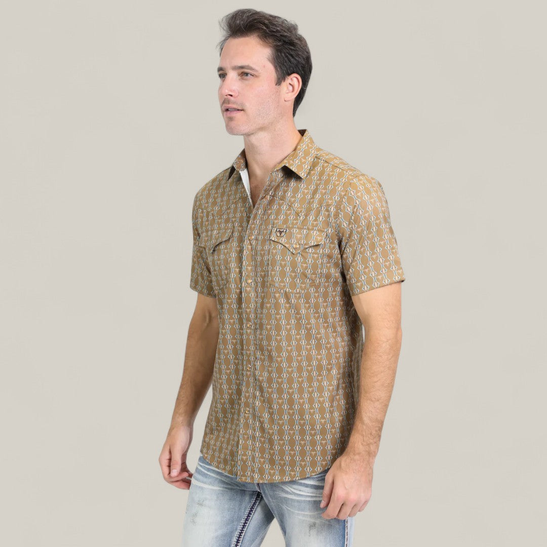 A man wears the Mens Performance Western Short Sleeve Aztec Print Camel Shirt (PGW10645) and light blue jeans, standing against a plain light background and facing slightly to the left.
