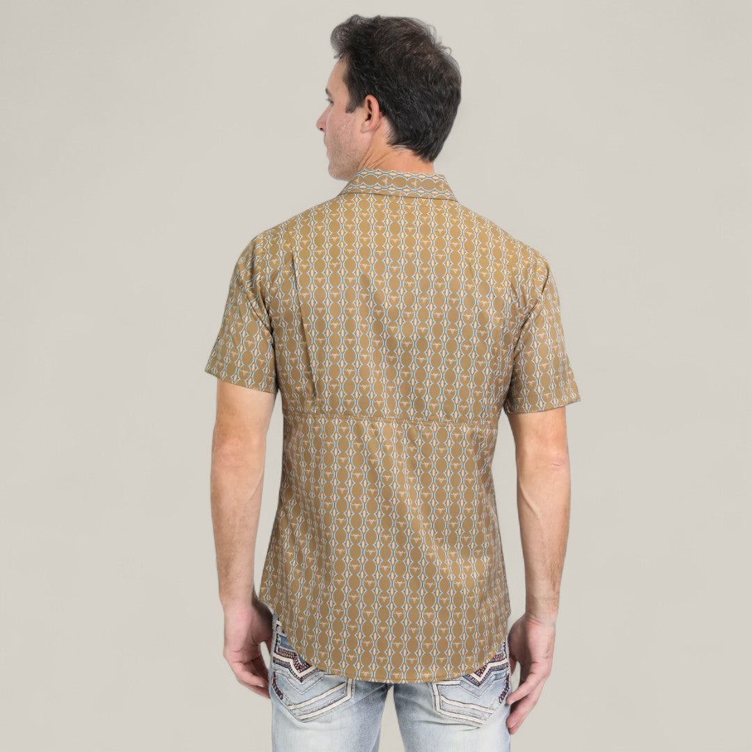 A man faces away from the camera, wearing the Mens Performance Western Short Sleeve Aztec Print Camel Shirt (PGW10645) paired with light blue jeans featuring decorative pocket stitching, set against a plain light background.