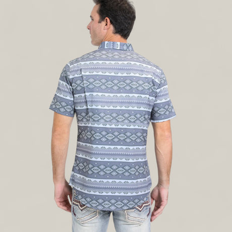 A man is shown from the back wearing a Mens Performance Western Short Sleeve Aztec Print Grey Shirt (PGW10649) with blue and white geometric patterns and light-wash jeans with stitched back pockets against a plain gray background.