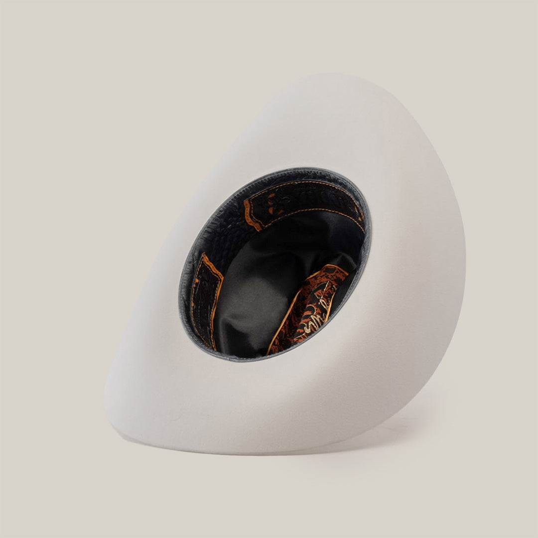 A 1000X Imperial White hat rests on its side against a plain background, revealing the dark brown and orange patterned interior with black lining, offering a glimpse of 100% genuine mink craftsmanship.