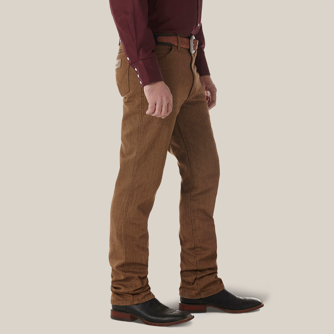 A person dressed in a maroon long-sleeve shirt, Wrangler Cowboy Cut Slim Fit Jean - 100936BKW, and black leather shoes with brown soles stands against a plain white background, wearing a brown belt with a silver buckle. The persons hands rest naturally by their sides.