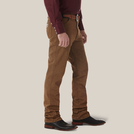 A person dressed in a maroon long-sleeve shirt, Wrangler Cowboy Cut Slim Fit Jean - 100936BKW, and black leather shoes with brown soles stands against a plain white background, wearing a brown belt with a silver buckle. The persons hands rest naturally by their sides.
