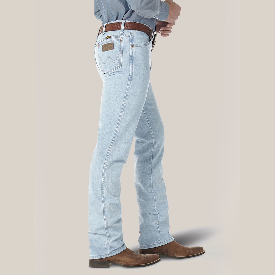 A side view shows a person in light blue Wrangler Cowboy Cut Slim Fit Jeans - 0936GBH, with a brown belt and cowboy boots, standing against a plain background. The jeans feature classic stitching on the back pocket.