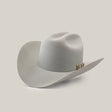 The 1000X Imperial Platinum is a light gray Larry Mahan cowboy hat with a wide brim, distinct crown crease, and decorative band with metal ornament, angled slightly on a plain backdrop, capturing the iconic western style.