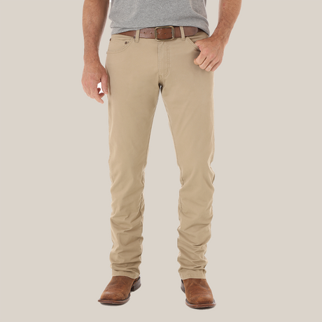 A person stands with their back to the camera, wearing a gray shirt and Mens Wrangler Retro Slim Fit Straight Leg Pant - 1088MWZFN in beige, noted for its visible pocket stitching and leather tag. Brown shoes complete the relaxed fit look.