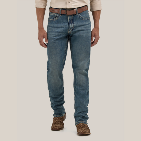 The lower half of a person is visible, wearing Wrangler Mens 20X Extreme Relaxed Fit Jeans - 1044MWXMA in Premium Denim blue with a worn look. The outfit is completed with a beige shirt, brown leather belt, and woven brown shoes against a plain background.