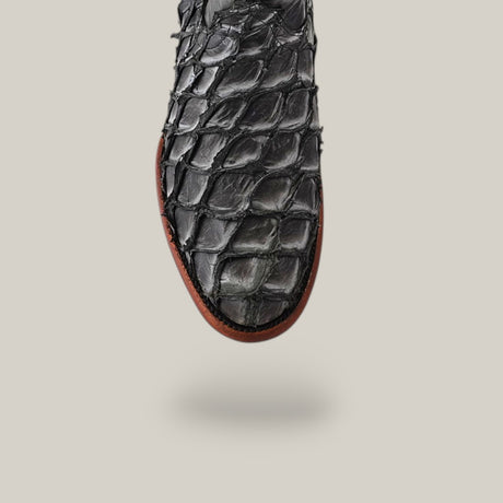 The Exotic Pirarucu Fish - Newspaper - Roper Toe showcases a textured black design crafted from luxurious Pirarucu fish leather with a reptilian scale pattern. Set against a light background, the contrasting brown leather sole highlights its elegance, ideal for luxury boot enthusiasts.