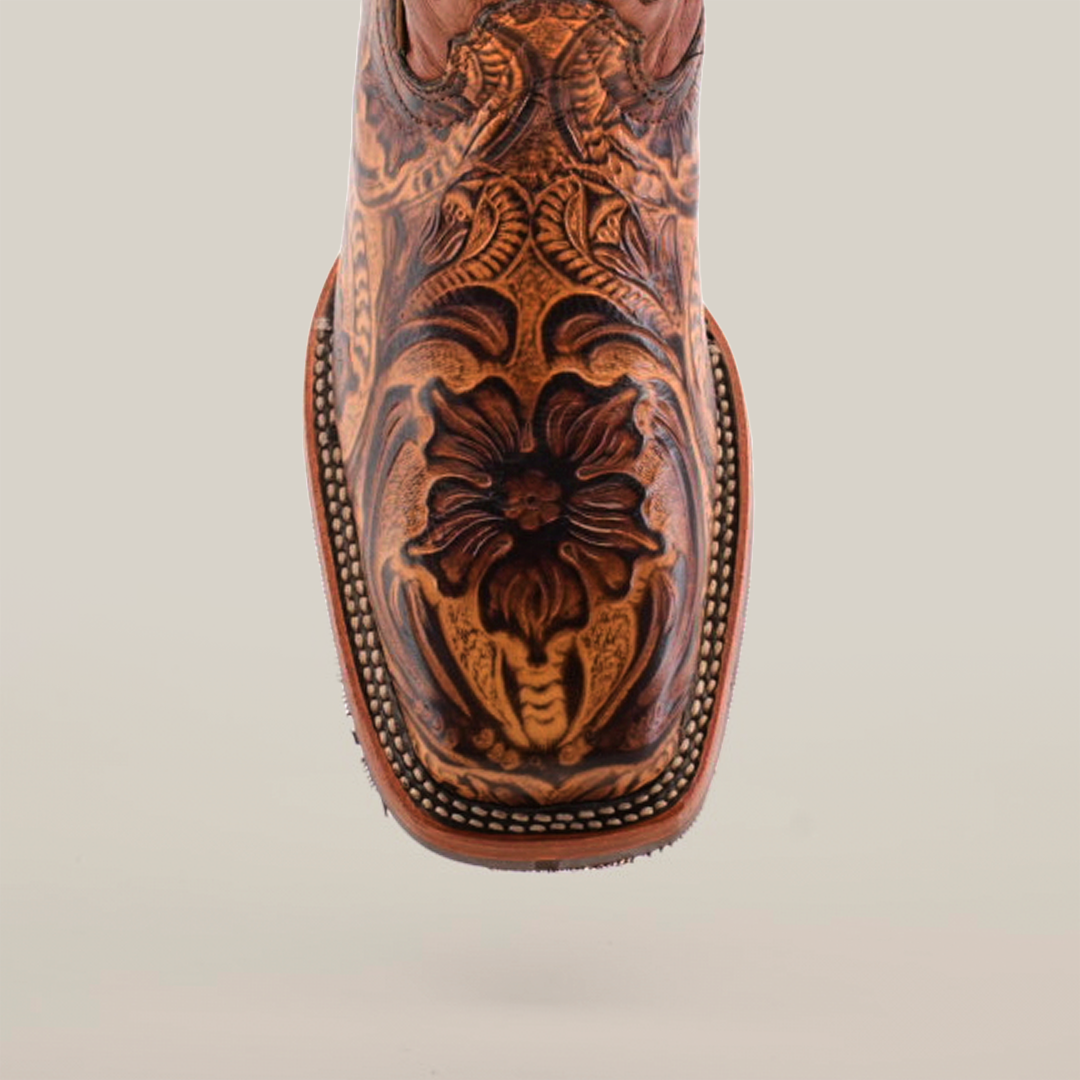 A close-up of the Handtooled Leave Orix boots showcases intricate floral and leaf designs on premium cowhide leather. It features a Rodeo toe with edge stitching and a slip-resistant sole, set against a plain white background.