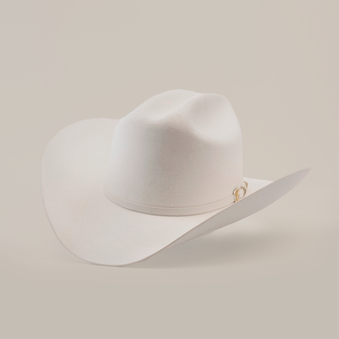 The 6X Real White hat is a luxury piece of Western headwear, featuring a wide brim and decorative band. Handcrafted from fur felt by skilled artisans, it is slightly tilted to accentuate its classic western style against a plain background.