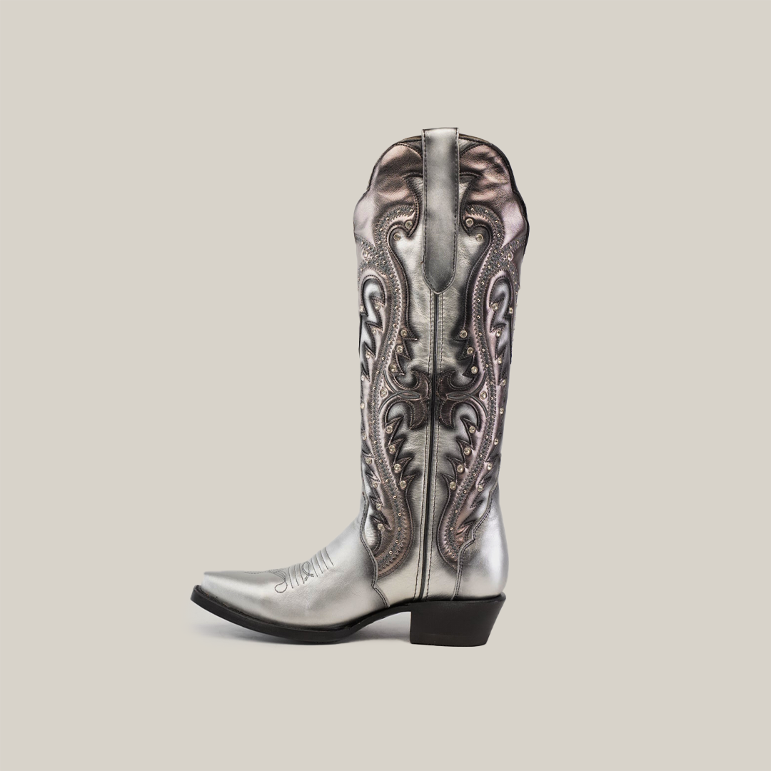 The Valentina Silver Tall Shaft boot, with a snip toe, is a stylish cowboy boot crafted from premium leather. It features metallic silver tones, elaborate embroidery, and ornate stitching with a mid-calf height and black heel against a plain light background.