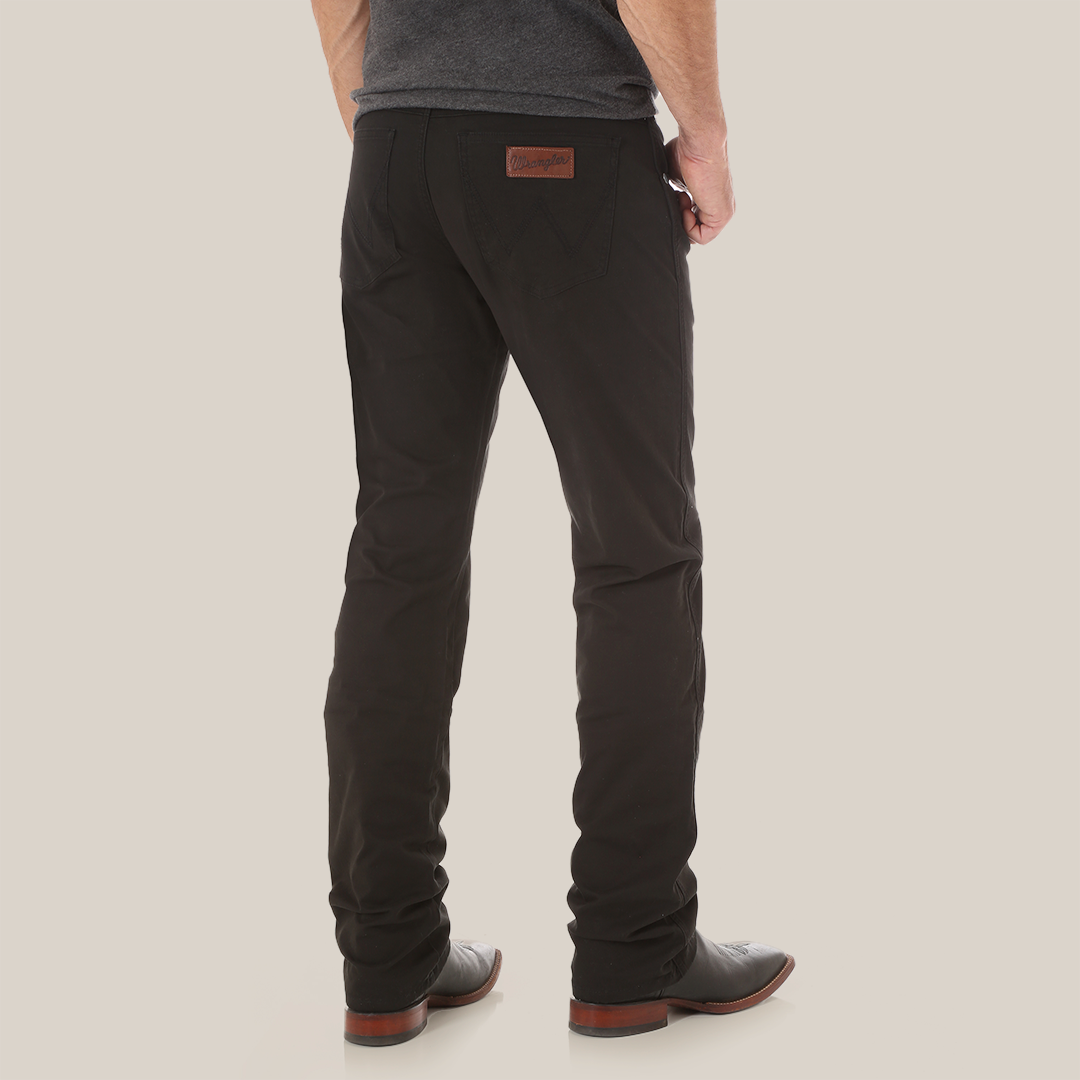 A person in Mens Wrangler Retro Slim Fit Straight Leg Pant - 88MWZBK and sleek black shoes stands facing away. These premium denim pants with a leather patch are paired with a dark gray shirt on a plain white background, showcasing a relaxed yet sophisticated style.