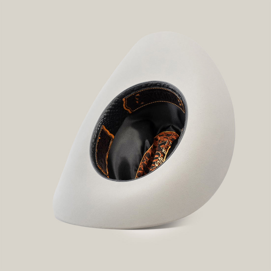 The 1000X Imperial Platinum is a modern, asymmetrical white hat with a wide brim, exuding sophistication. Its interior features stylish black and orange patterns, redefining the essence of a classic Western hat against a plain white background.