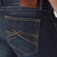 A close-up shows a person in Mens Wrangler 20X No. 42 Vintage Bootcut Jeans. These dark blue slim fit jeans boast tan stitching with intricate patterns on the right back pocket and a brown leather logo patch on the waistband, perfectly complementing a green shirt.