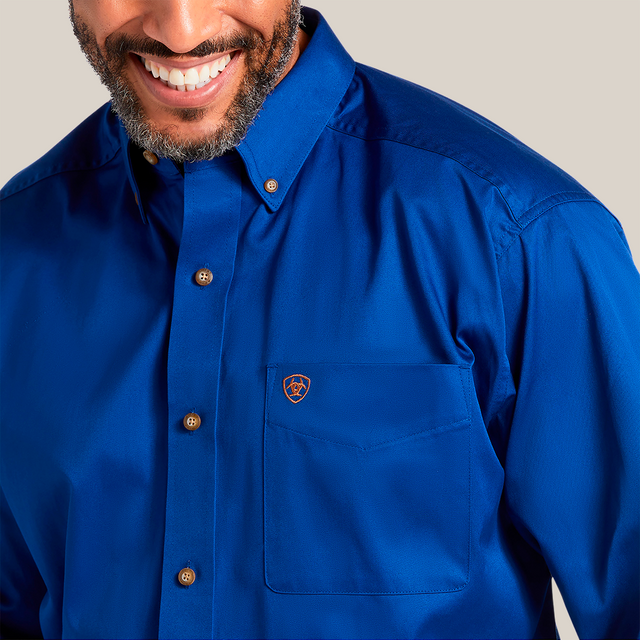 A person smiling in a Solid Twill Classic Fit Shirt Blue - 10006660, made of 100% cotton twill, with brown buttons and a small emblem on the pocket. The smart collar adds to its charm. Image highlights the upper chest and part of the face.