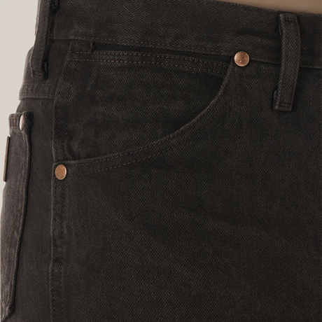 Close-up of someone wearing Wrangler Cowboy Cut Slim Fit Jean - 0936KCL in dark green with copper rivets, featuring a front pocket and belt loop. A brown shirt is neatly tucked in.