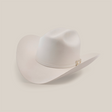 The 10X Jerarca White is a beige cowboy hat made from fine fur felt, featuring a wide brim and a decorative band around the crown. This classic western headwear, reminiscent of Larry Mahan 10X style, is presented against a plain white background.