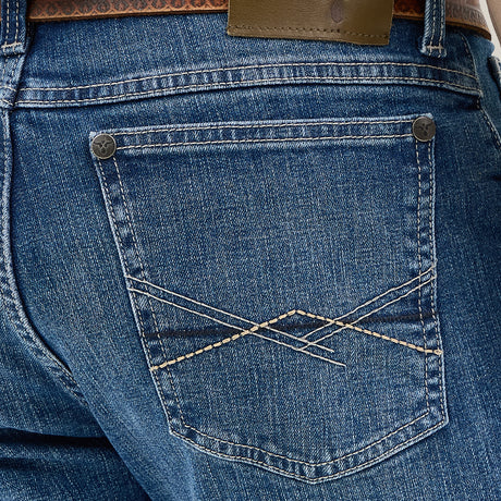 Close-up of a person wearing Mens Wrangler 20X No. 42 Vintage Bootcut Jeans, identifiable by their decorative stitching and Wrangler patch on the back pocket, secured with a brown patterned leather belt.