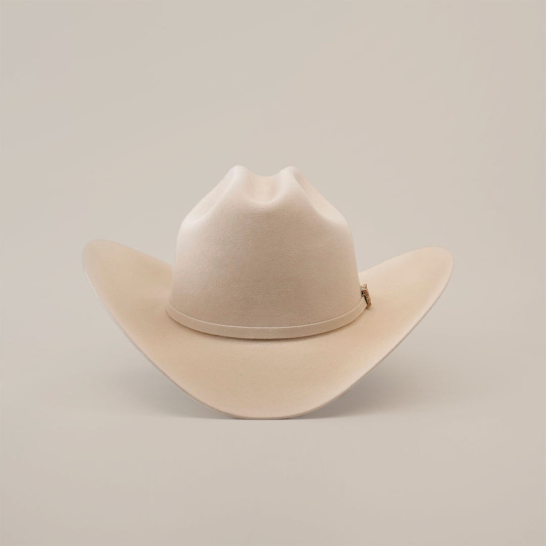 The 100X Independencia Belly, a beige cowboy hat made of premium full beaver fur, features a wide brim and a stylish crown crease, elegantly displayed on a plain white background.