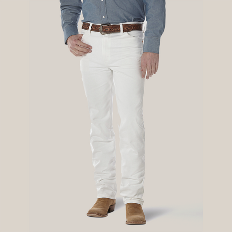 A person wearing a blue button-up shirt, Wrangler Cowboy Cut Slim Fit Jeans (0936WHI), and a brown leather belt is grounded in brown suede shoes. The iconic Wrangler patch enhances the look against the plain white background.