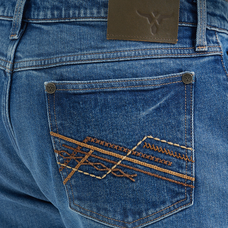 A close-up shows the back pocket of Wrangler 20x Mens Medium Wash Backwater Vintage Stretch Jeans, featuring an orange and brown embroidered geometric design. A logo leather patch is on the waistband. The jeans pair classically with a tucked plaid shirt for a timeless style.