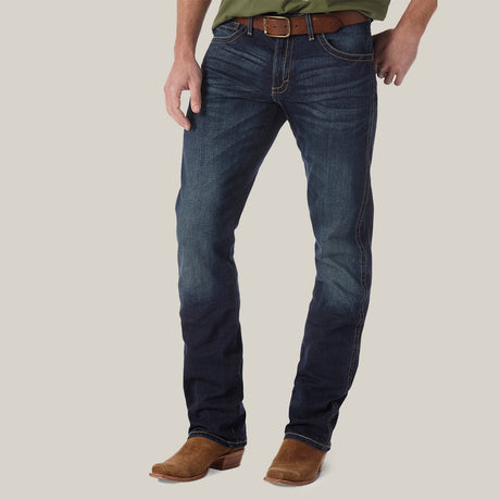 A person in Mens Wrangler 20X No. 42 Vintage Bootcut Jeans and brown boots stands against a plain background, featuring faded premium denim and a sleek brown leather belt, with their top part not visible.