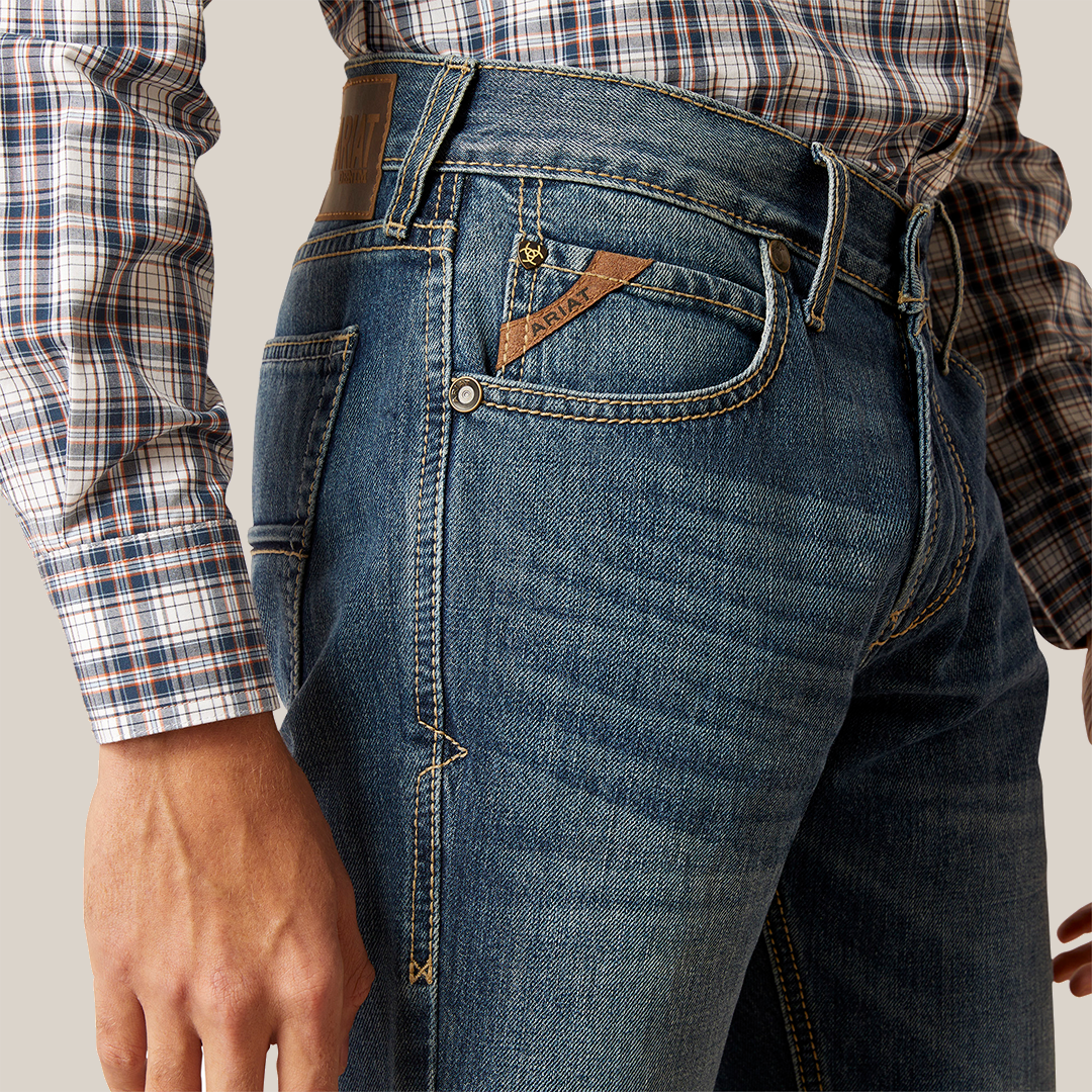 Wearing premium denim M7 Slim Ezra Straight jeans with visible stitching and a brown leather patch, paired with a plaid shirt, captures the essence of casual elegance and the modern cowboy look.