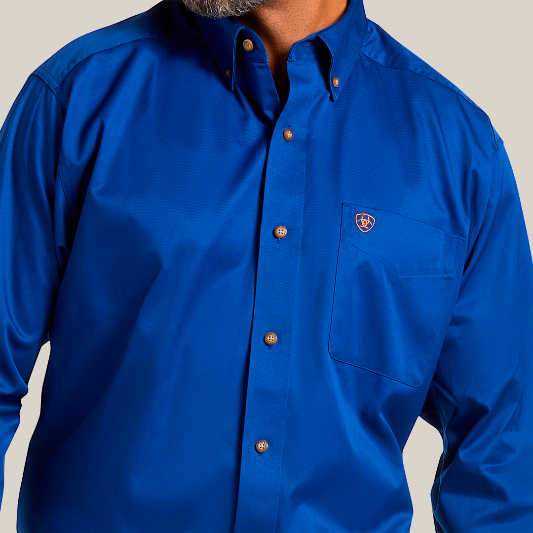 A person smiling in a Solid Twill Classic Fit Shirt Blue - 10006660, made of 100% cotton twill, with brown buttons and a small emblem on the pocket. The smart collar adds to its charm. Image highlights the upper chest and part of the face.