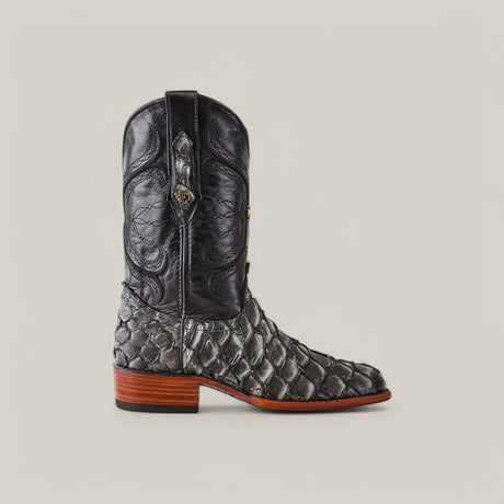 The Exotic Pirarucu Fish - Newspaper - Roper Toe boot showcases a tall black leather shaft with intricate stitching, scalloped scales resembling exotic Pirarucu leather on the lower part, a wooden heel, and roper toe against a plain backdrop.
