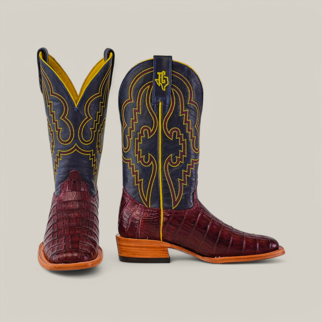 The Exotic Caiman Belly Tail Cowboy Boots in Wine showcase a dark and light brown design against a grey backdrop. Crafted from exotic leather, they feature intricate yellow stitching, wooden heels, and a square toe. The shaft is lined with yellow and embossed with the logo.