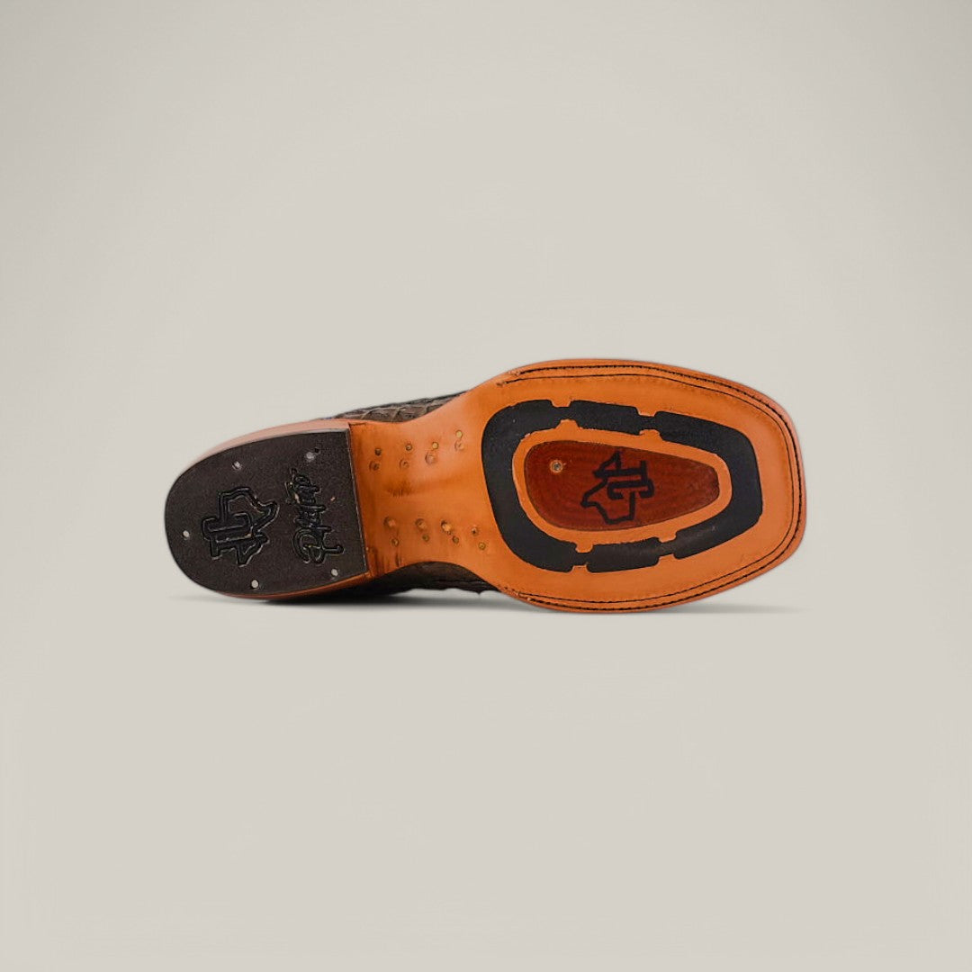 The image reveals the sole of an Exotic Caiman Belly Tail shoe, Gray with a Square Toe, featuring a unique Western-style pattern. The textured grooves, stylized logo initials, and contrasting tan and black colors highlight the refined craftsmanship typical of exotic leather designs.