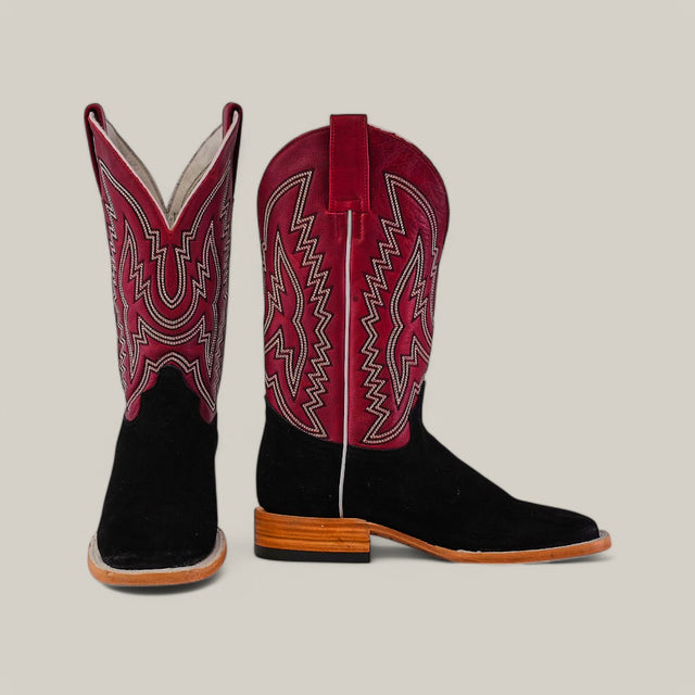 The Black Suede - Platinum - Square Toe boots feature black suede lower sections and red upper shafts with intricate white stitching and zigzag patterns. Platinum accents add elegance, complemented by a wooden heel against a plain beige background.