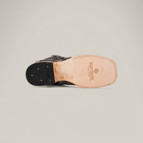 The Exotic Pirarucu Fish cowboy boot, in gray with a square toe, features a light tan sole branded USA Country, a dark textured heel, and is made from sustainable materials. It is displayed against a plain light gray background.