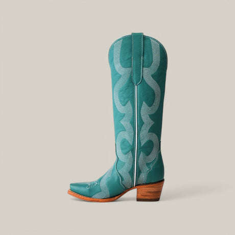 The Olimpia Green Teel cowboy boot features premium materials, with intricate lighter teal stitching and a pointed snip toe. The tall shaft displays an elaborate pattern against a plain background, highlighting the craftsmanship of the wooden heel.
