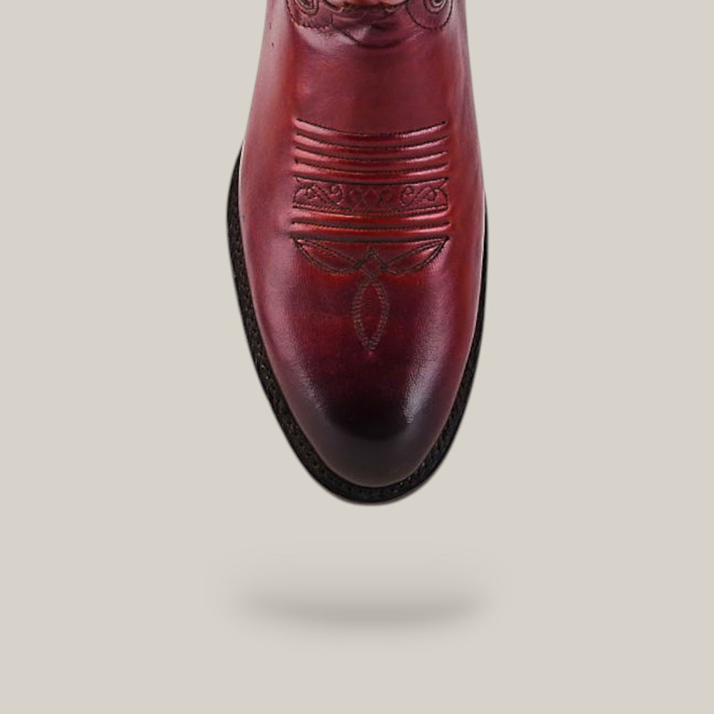 A top view of the Wyatt - Cogñac - Roper Toe boot, a reddish-brown cowhide design featuring decorative toe stitching, highlights its quality craftsmanship against a plain light background.