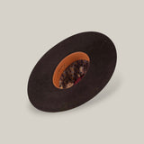 The 10X Grizzly - Tacchino luxury hat, with a wide black brim, is displayed upside down to reveal its brown leather inner band and paisley-patterned lining against a plain beige background.