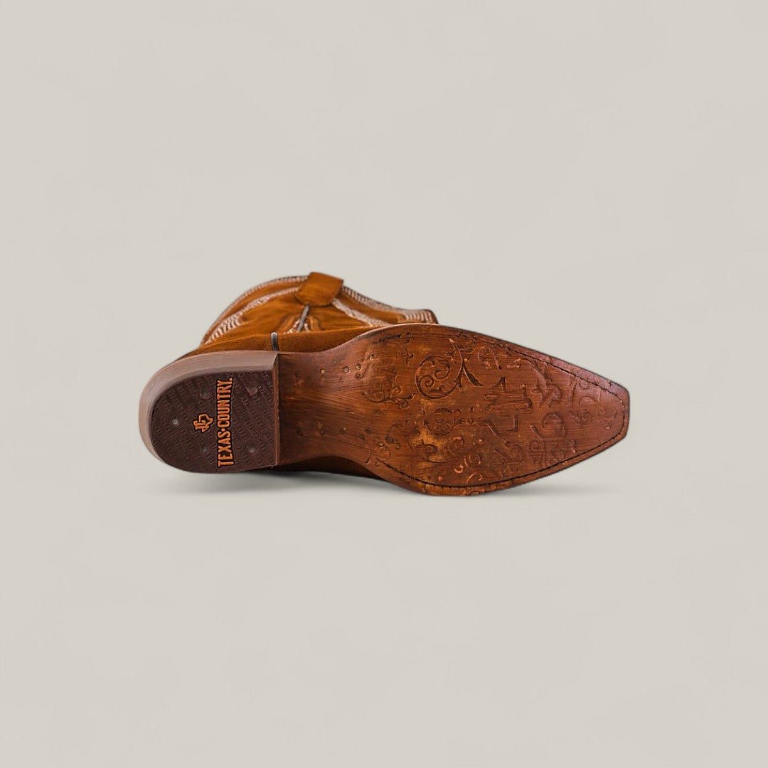 The Daisy Camel - Tall Shaft - Snip Toe boot, crafted in brown leather, is displayed on its side to reveal an intricately embossed sole featuring TEXAS COUNTRY by the heel against a plain light beige background.