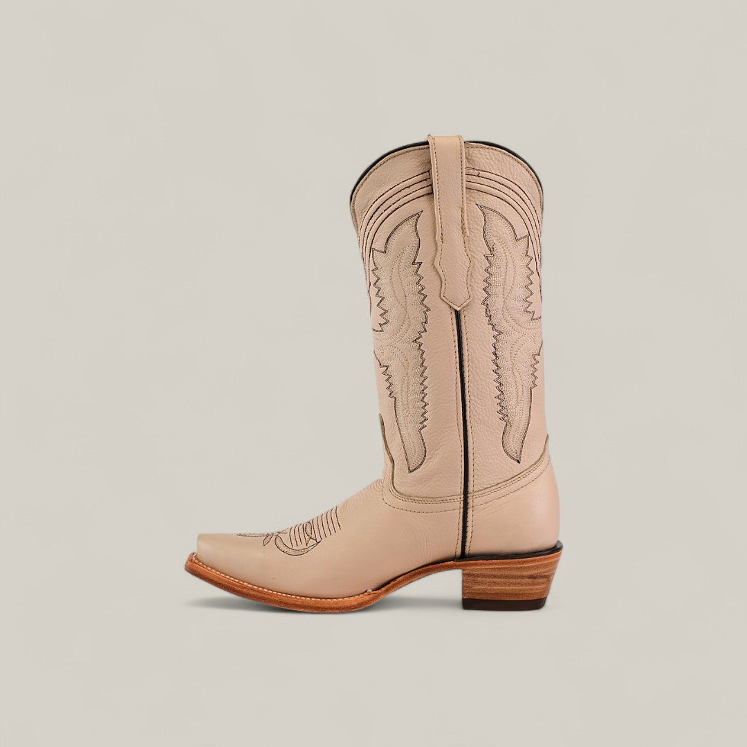 The Tessa Champagne Mid Shaft Snip Toe boot features light beige color, decorative stitching, a wooden stacked heel, and a pull tab—shown in profile against a light background—for women who value style and comfort.