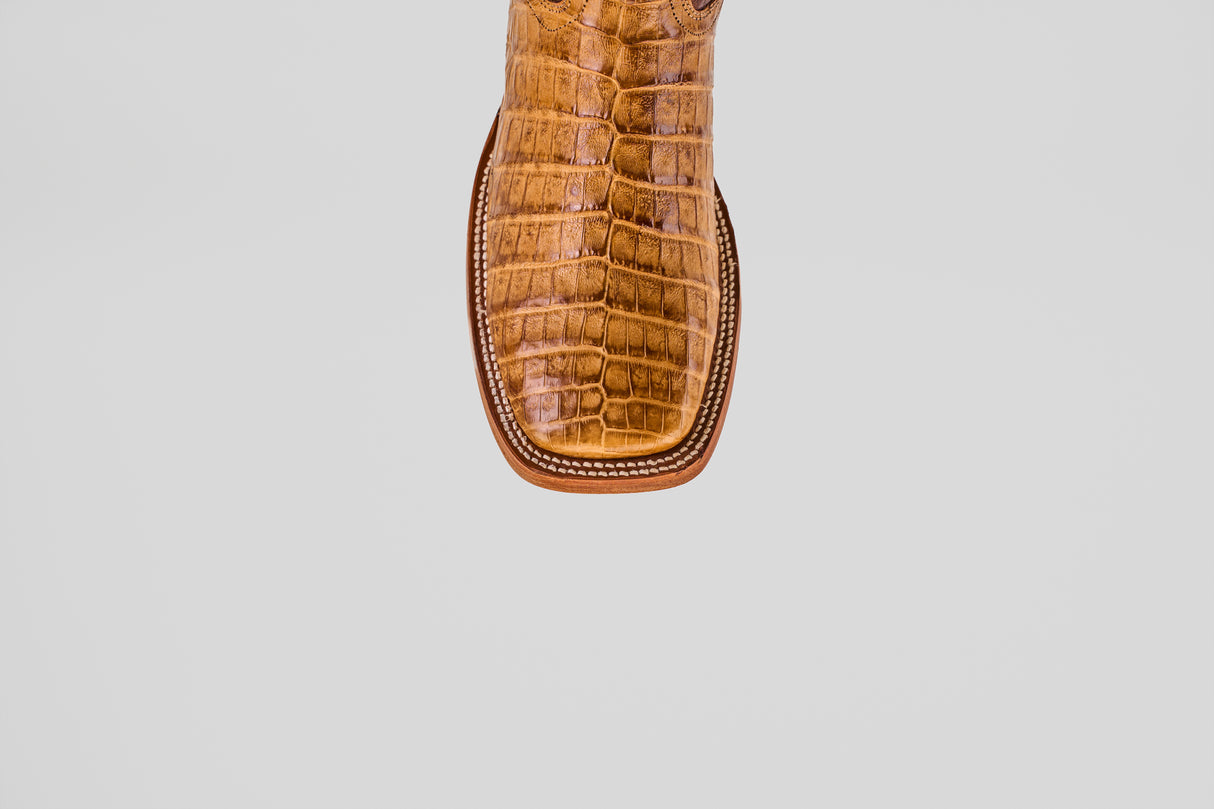 A close-up of the Exotic Caiman Belly - Camel - Square Toe boot shows its brown caiman leather with a textured, crocodile-like pattern and square tip, set against a plain white background.