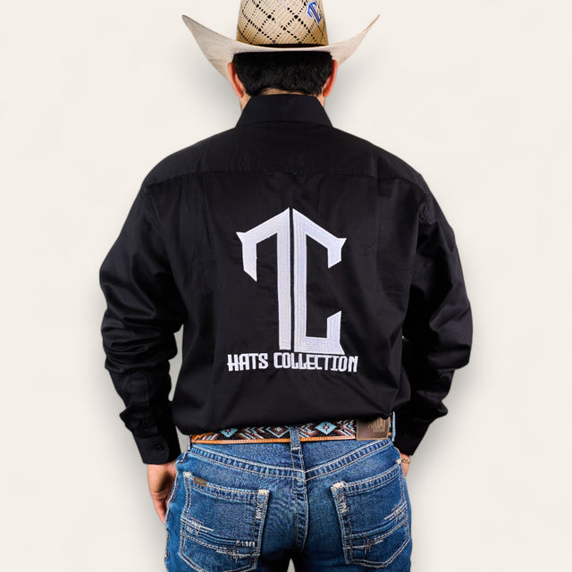 Wearing the TC Hats - Black & White premium black button-up shirt with "TC HATS COLLECTION" in large white letters on the back, blue jeans, and a tan cowboy hat, a person stands against a plain light background.
