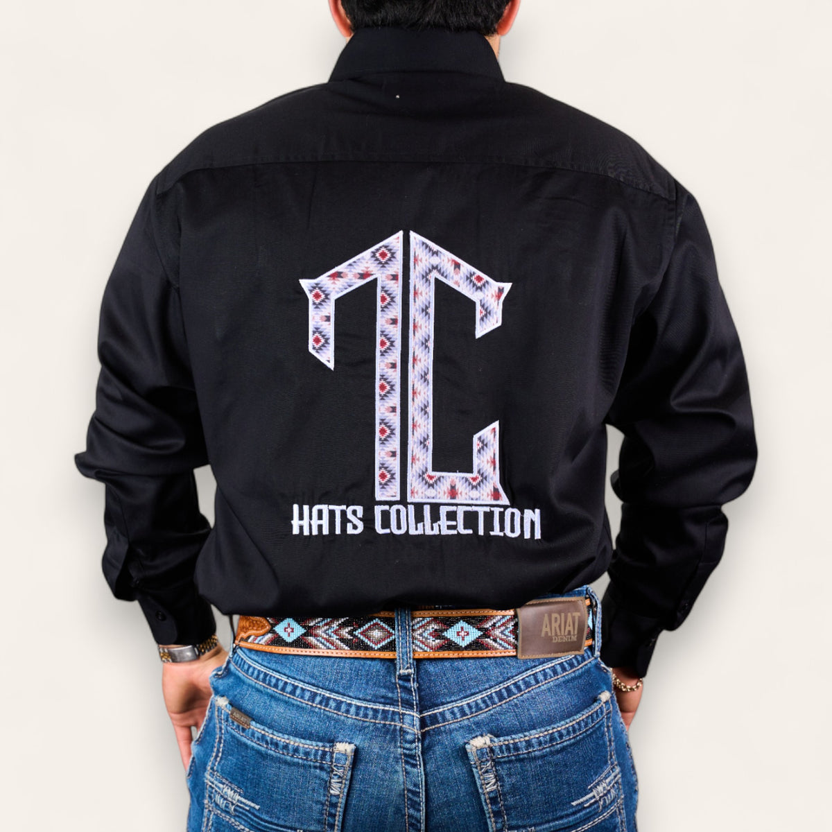 Someone wearing the TC Hats - Black Red Aztec shirt with a patterned TC logo embroidered on the back, styled with blue jeans and a matching patterned belt.