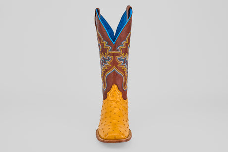 The Ransom - Buttercup - Square Toe Boot features a yellow exotic full quill ostrich leather foot and a brown shaft with blue and yellow stitching, shown on a plain light gray background.