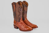 The Exotic Full Quilt Ostrich - Brandy - Round Toe boots feature handcrafted, textured ostrich leather with decorative stitching on tall, darker brown shafts, displayed against a plain light gray background.