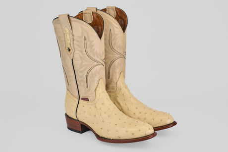 The Exotic Full Quilt Ostrich - Bone - Round Toe boots feature textured genuine ostrich leather in light tan, decorative stitching on the shaft, pull straps at the top, and brown wooden heels.