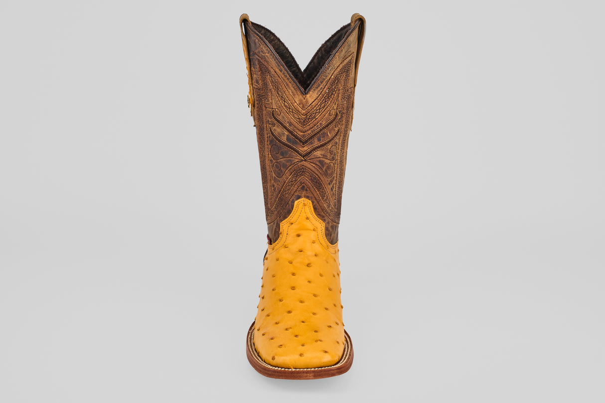 The Exotic Full Quilt Ostrich - Buttercup- Square Toe features a yellow ostrich leather foot and a tall, brown, intricately stitched shaft—shown facing forward on a plain gray background—for handcrafted western boot enthusiasts.