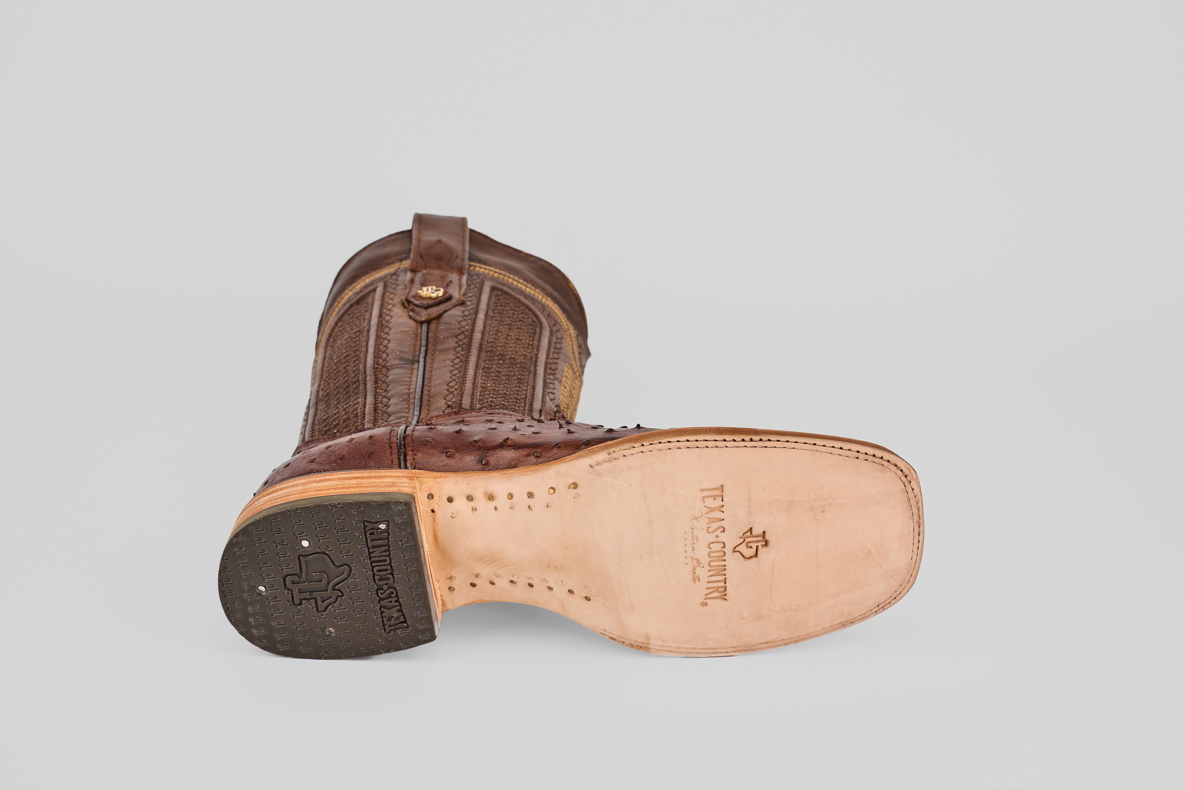 The Exotic Full Quilt Ostrich - Brown - Square Toe boot features a textured upper, smooth sole with TEXAS COUNTRY branding, a black textured heel, and classic cowboy style—ideal for square toe boot fans.