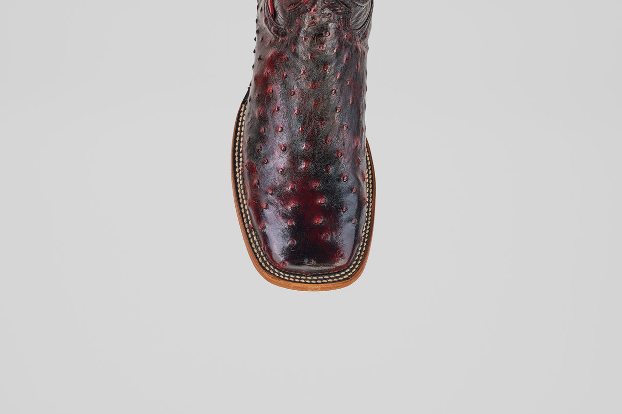 Close-up of the toe of the Exotic Full Quilt Ostrich - Black Cherry boot, featuring a square tip, textured dark red leather, decorative stitching, and a light brown sole, set against a plain white background.