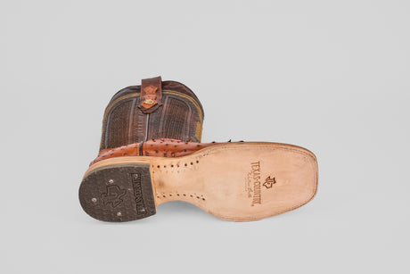 The Austin - Brandy - Square Toe cowboy boot lies on its side, displaying a textured leather upper, decorative stitching, a leather sole with metal toe cap, and “Texas Country” stamped on the bottom.